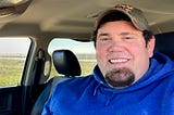 A portrait of a man in a hat with a blue sweater