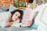 woman relaxing in bed & reading a book, with bookshelves in the background