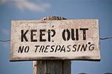 A sign board on a fence which says, “Keep Out No Trespassing”.