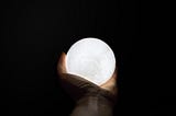 A hand holding a glowing orb against a black background.