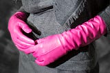 Torso of woman wearing black with elbow length pink leather gloves clasped in fron-nt of her.