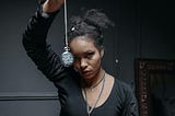 Young woman with an intense stare, dressed in black, dangling a blurry watch on a long chain in front of her face