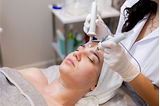 A young woman lies on a beautician’s table during a microcurrent treatment procedure