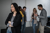 a woman looking annoyed while people gossip behind her back