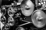 a black and white photo of a bunch of gears that seem to be part of a machine of some kind. it is unclear from the photo what kind of machine it is or what its purpose or function is.