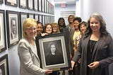 Sarah Eubanks holds official portrait of her daughter, Rachael with SOM employees in the Hall of Treasurers.