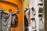 Image of part of the inventory of Greek/Roman statues in the Sloan museum in London. In the left part, against an orange background, the statue is holding a microphone which has been drawn into the original photograph