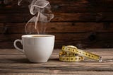 A steaming cup of coffee placed strategically next to a measuring tape with a significant amount of slack.