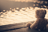 teddy bear sitting at a pond watching the sun set