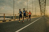 four people running across a bridge