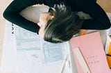 woman with her head on a desk, looking stressed, on top of jumbles of documents