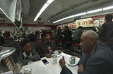 Two older black men and a young boy sit around a table, deep in conversation at Ben’s Chilli Bowl in the USA.