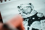 Photo of someone drawing an astronaut on a sheet of paper.