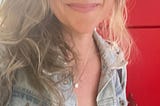 author blonde hair, jean jacket, red wall