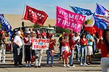 Trump supporters carrying flags and wearing MAGA attire at a rally.