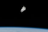 Astronaut EVA above Earth. The astronaut appears to be alone in the deep black of space, and only the implicit existence of the photographer suggests otherwise.