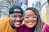 A young, Black couple smiling for the camera at Allan Gardens in Toronto, Canada