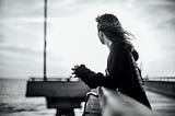 black and white photo of the author standing on a pier, looking out over the ocean