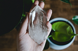 Hand holding a large, colorless crystal, near a plant.