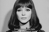 A screenshot from Jean-luc Godard’s Alphaville. A woman with shiny black hair and thick mascara stares into the camera. The subtitle reads: Away, away, says hate; Closer, closer, says love.