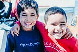 Two young boys smiling at the camera with arms around each other’s shoulders