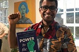 Danny, smiling, fist raised in ‘solidarity’ holding a copy of his book.
