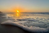 Sunrise over the Atlantic ocean in the background with sea foam in the foreground