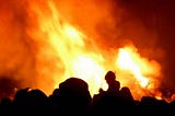 A crowd of people in silhouette, standing in front of a raging bonfire.