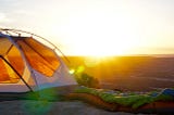 A sunrise across a valley , with a tent in the foreground