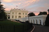 The US White House seen from the west with a sunset behind it.