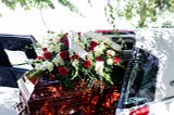 funeral details of flowers on cherry wood casket and white car