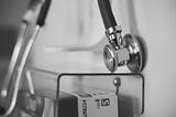 A black and white photo of a stethoscope hanging on a wall in a nondescript healthcare setting.