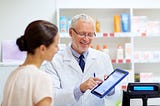 A pharmacist pointing something out to a customer on a tablet.