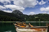 brown and white boat on lake near green mountain under blue and white cloudy sky during