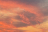 Photo of sky at sunset with swirling orange pink clouds tinged with grey