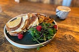 Excellent photo of a cheese toastie,on a wooden table, with a coffee in the background artfully blurred from view