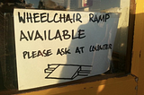 Hand-written sign in a store window reads: wheelchair ramp available please ask at counter