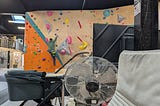 A pram in the foreground, inside of a climbing gym. In the background, a man is halfway up the climbing wall.