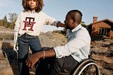 A fashion shoot featuring two people wearing Tommy Hilfiger Adaptive. The man is in a wheelchair & a woman appears to have a bionic arm.