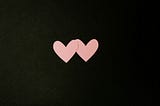 Two pink paper hearts on a black background