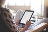 Person reclines on a chair, reading on a tablet or e-reader