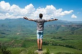 A man opens his arms wide before a vista, representing the world at his fingertips