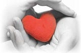 Two hands tenderly holding a red heart