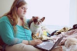 A person sat on their bed using a laptop, with their dog sat next to them