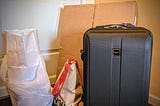 A large box, plastic bag, paper bag, canvas bag and hard suitcase are all grouped together