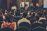 An audience listens to a speaker panel at an event.