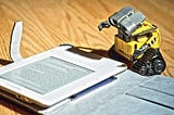 toy robot looking like it is reading from a Kindle device