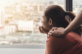 Picture of a woman staring out of the window with someone putting their hand on her shoulder
