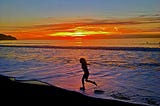 Little girl runs through a wave at sunset.