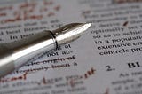 Photo shows closeup of a pen sitting on a printed document covered in edits written in red pen.
